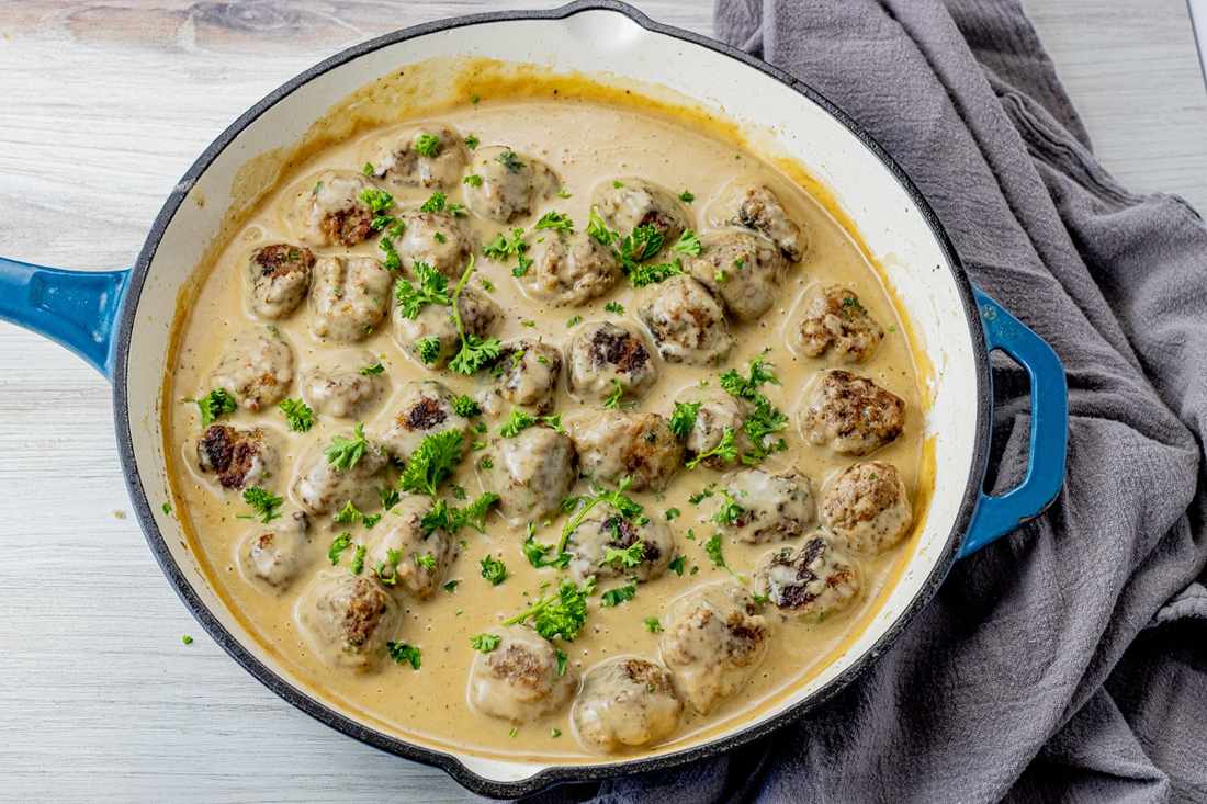 Enameled Dutch oven pot filled with slow-braised Swedish meatballs bubbling in thick cream gravy