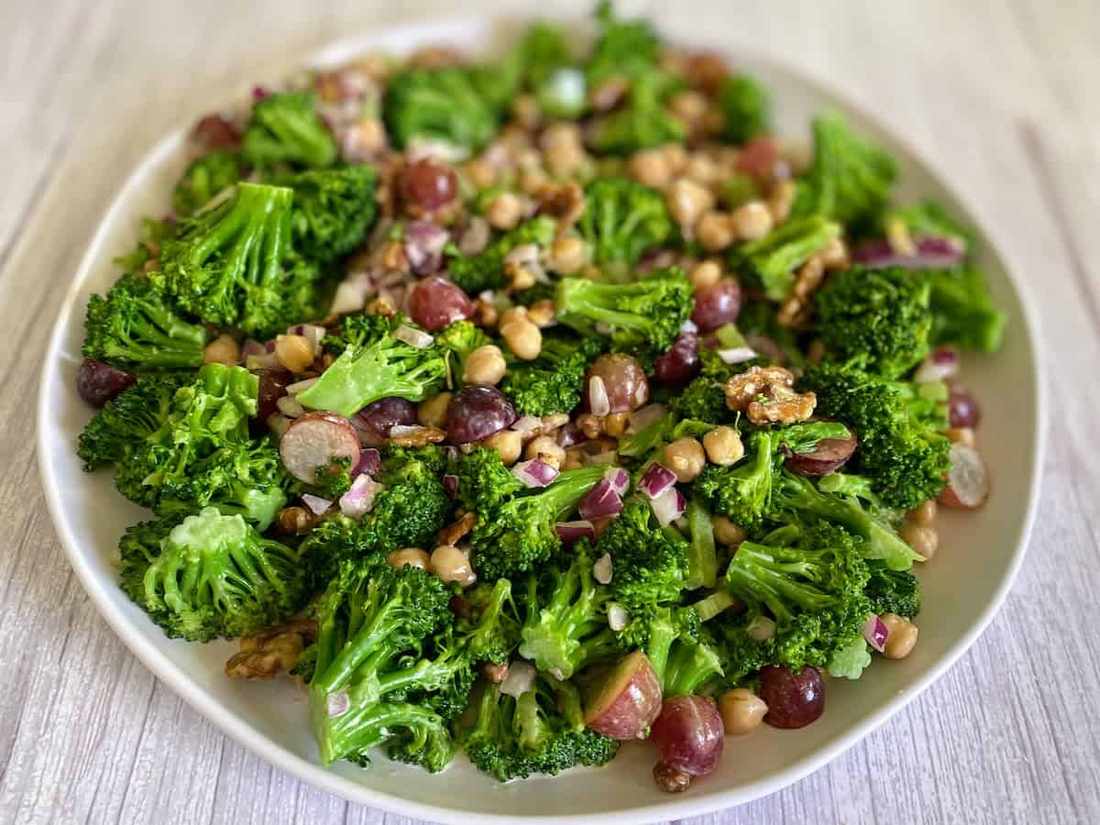 Vegan broccoli salad with florets, avocado‑lime dressing, pumpkin seeds, dried cherries, and vegan cheese crumble