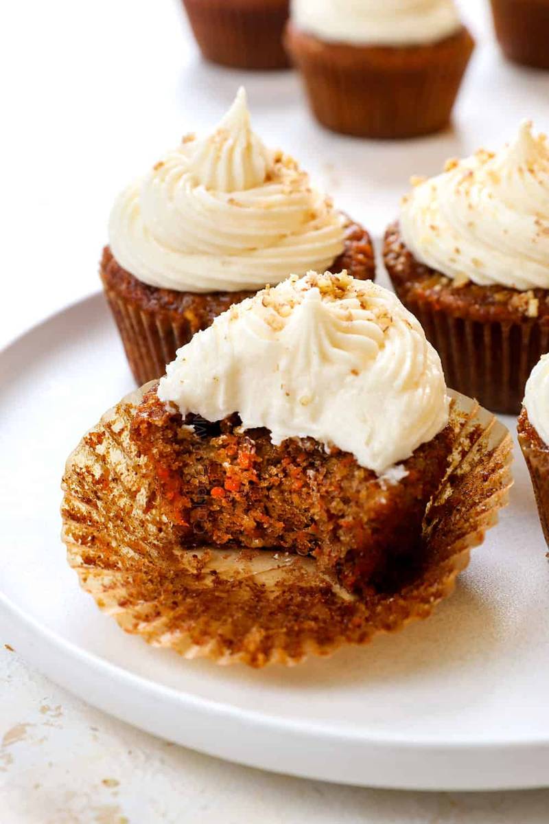 Carrot cupcakes topped with swirled pink and white cream cheese frosting and a dusting of cinnamon