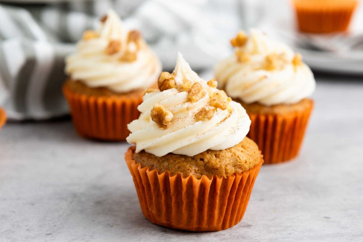 Homemade carrot cupcake topped with fluffy cream cheese frosting, moist spiced crumb, and a pinch of cinnamon