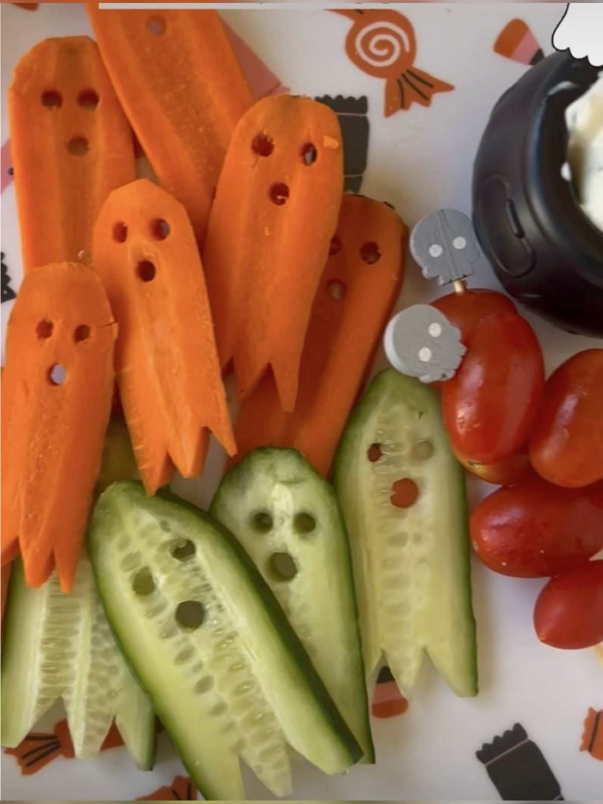 Sliced cucumbers and carrots shaped like ghosts with olive eyes and cream cheese dip.