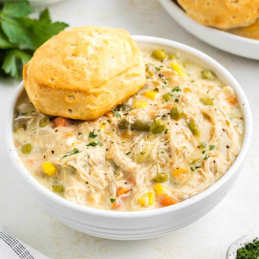 Creamy chicken pot pie soup featuring chicken, peas, carrots, potatoes, and herb‑infused biscuit topping