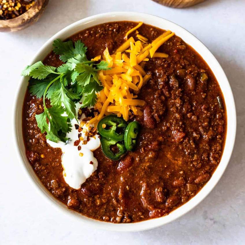 Robust Dutch oven beef chili with beans, melted cheese, sour cream, jalapenos, beer‑infused broth