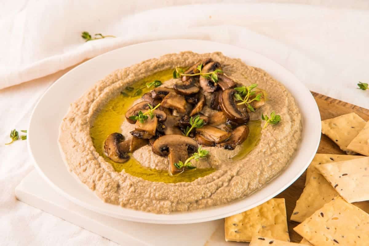 Warm, earthy mushroom dip in a rustic bowl surrounded by crisp crackers and herbs