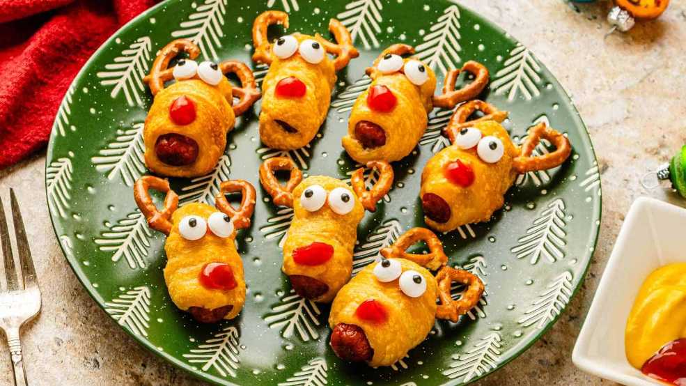 Mini hot dogs wrapped in pastry, topped with pretzel sticks as antlers, arranged like reindeer