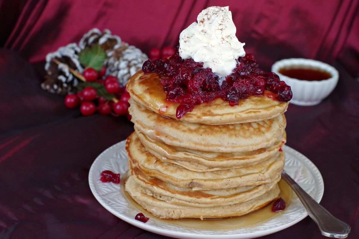 Stack of golden pancakes topped with glossy cranberry compote and a dusting of powdered sugar
