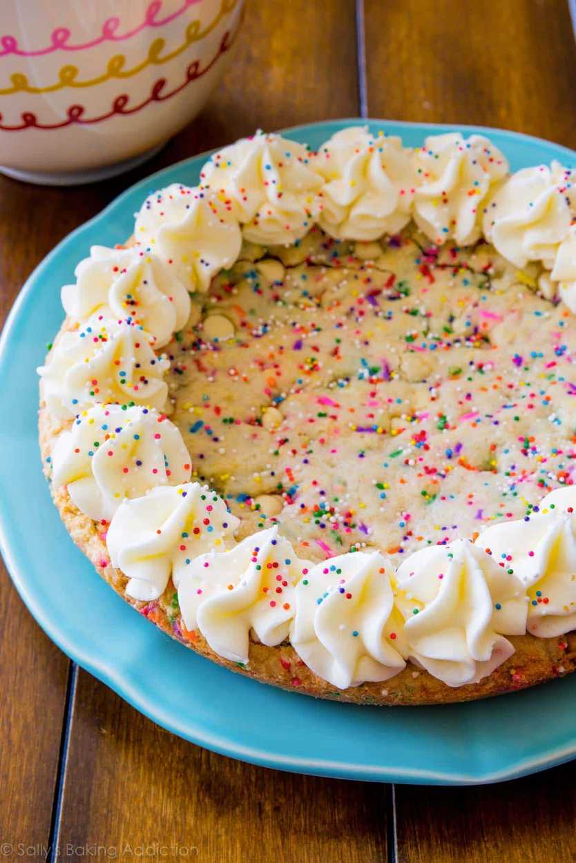 Brightly speckled giant cookie cake topped with whipped frosting and rainbow sprinkles