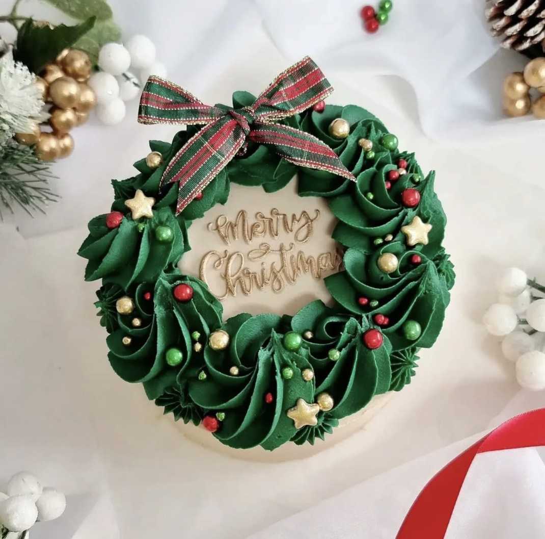 White vanilla cake shaped as a wreath, wrapped in green buttercream and pine needle decorations