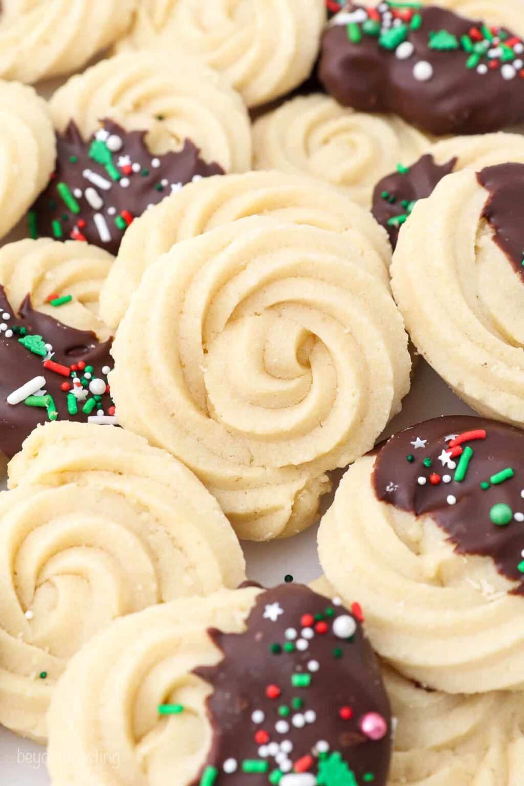 White butter spritz cookies dipped in dark chocolate with a festive red drizzle on a white tray.
