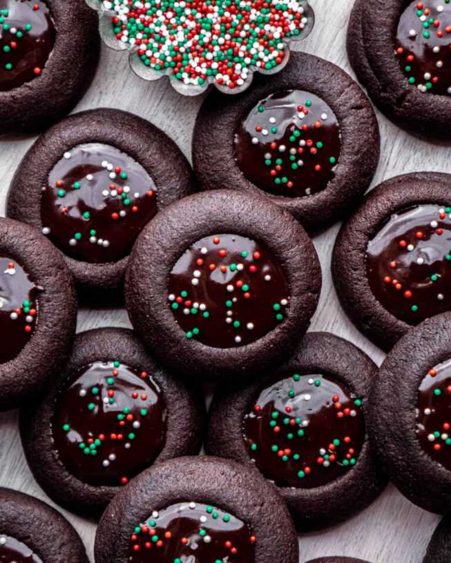 Dark chocolate thumbprint cookies filled with glossy fudge, dusted with cocoa powder on a festive red plate.