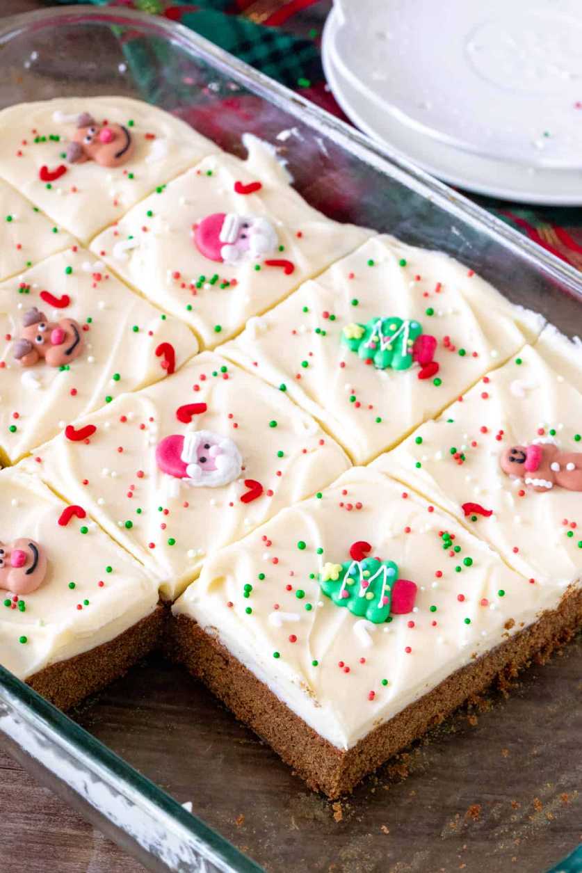 Square gingerbread bars topped with white icing and red sprinkles on a wooden board.