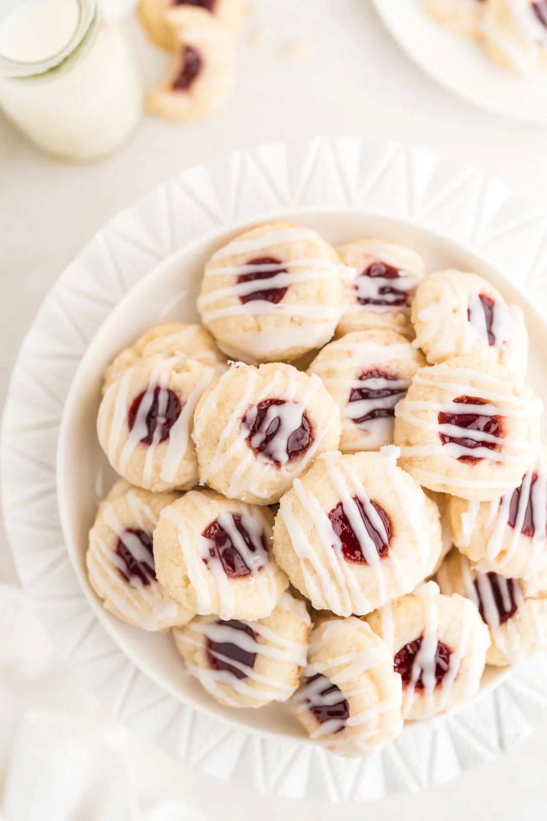 White sugar cookies with raspberry jam centers and a delicate white glaze on a wooden board.
