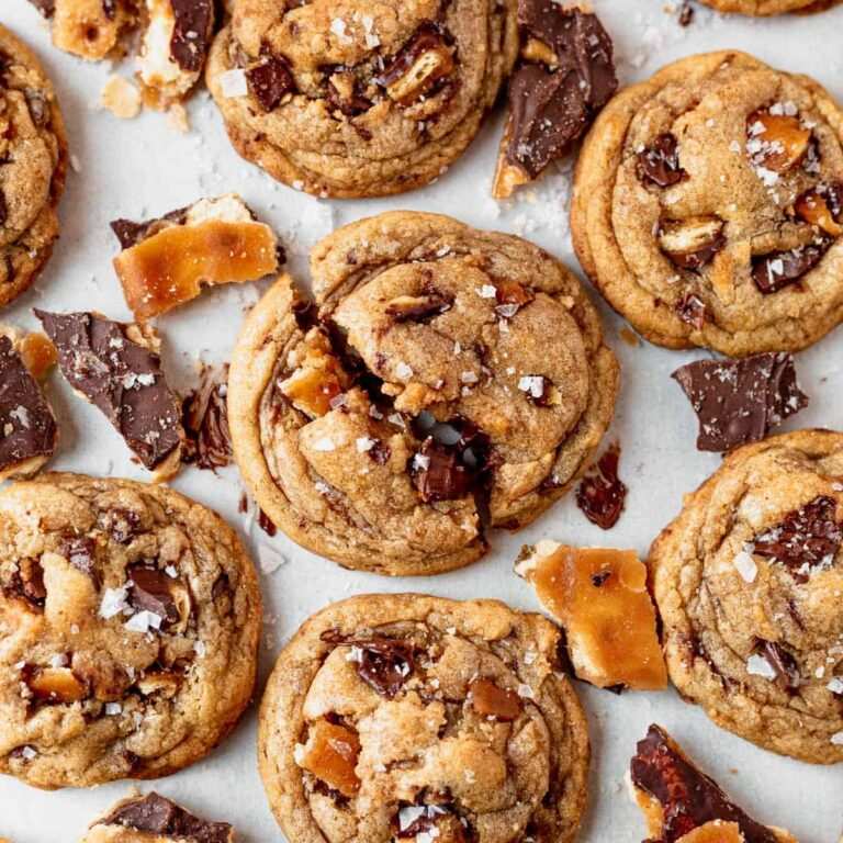 Thick chocolate chip cookies with toffee bits and a sprinkle of flaky sea salt on a wire rack.