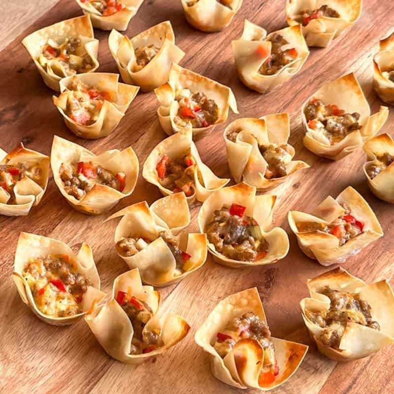 Golden wonton cups filled with spicy sausage and melted cheese, topped with chives