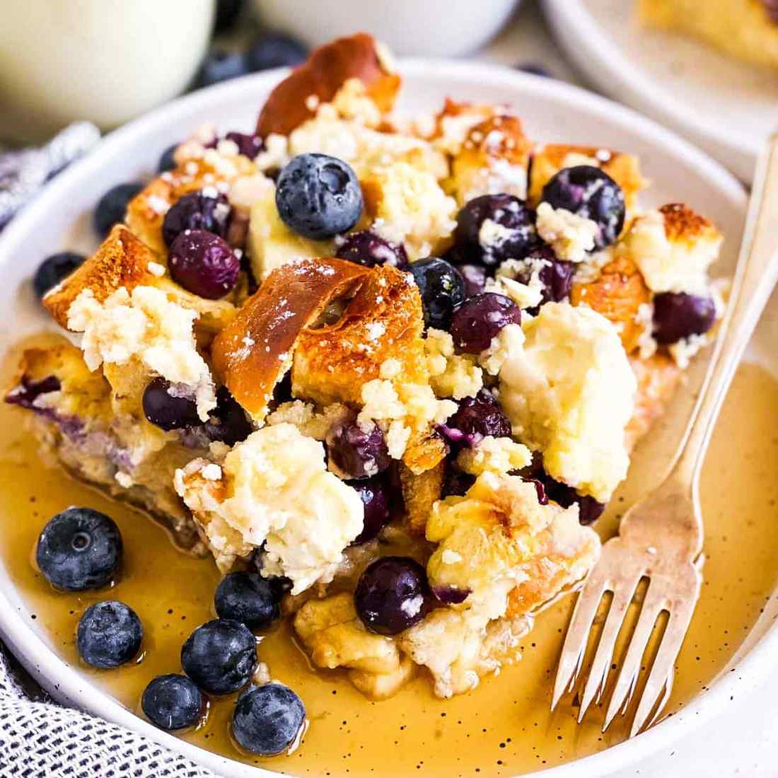 Lush blueberry‑speckled golden casserole, custardy bread cubes, sweet berry glaze, inviting breakfast delight