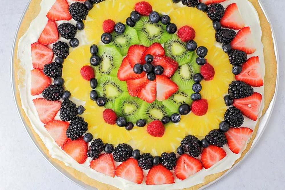 Sugar cookie fruit pizza with cream cheese frosting, papaya cubes, passion fruit pulp, and kiwi