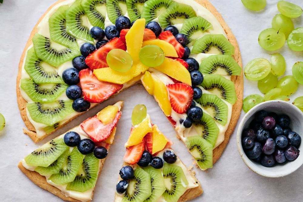 Classic sugar cookie crust topped with cream cheese frosting, fresh strawberries, kiwi, and blueberries, vibrant summer dessert