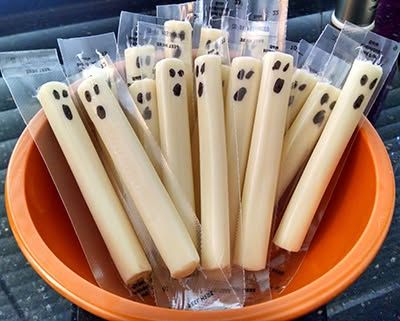 Pre‑packaged string cheese sticks painted with white chocolate “ghost” faces and black licorice eyes.