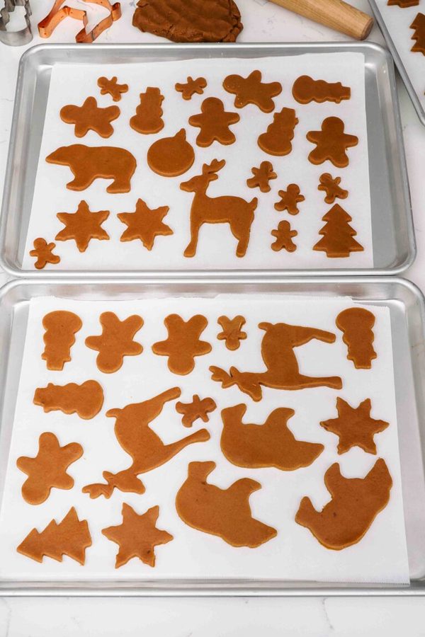 Unbaked shaped gingerbread cookies on parchment trays, warm spices, festive shapes
