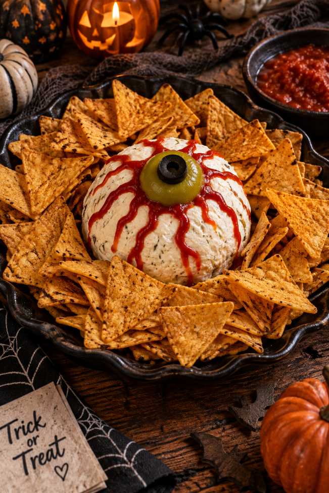 Large cheese ball decorated with red pepper jelly veins and black olive pupils on a white plate