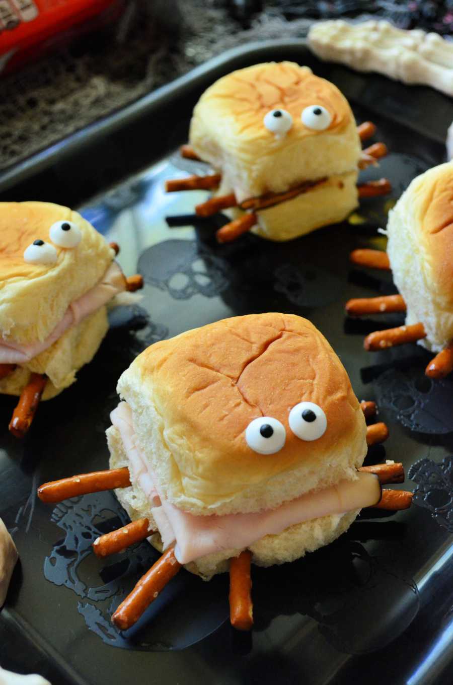 Mini turkey burgers on buns with cheese and a spider web made of cream cheese