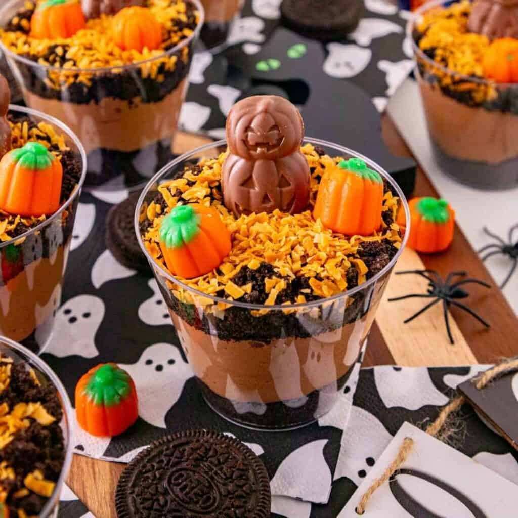 Clear dessert cups layered with rich chocolate pudding, crushed Oreo dirt, gummy worms, and Milano tombstone cookies.