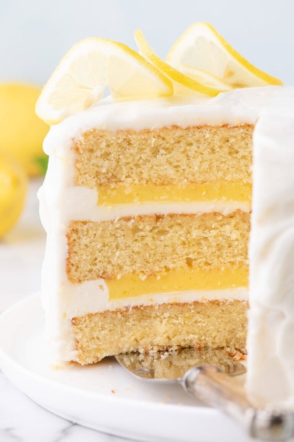 Three‑layer lemon curd cake, bright yellow layers, topped with whipped cream and candied lemon peel