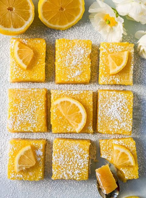 Thick lemon bars dusted with powdered sugar, bright yellow, on a rustic plate with a fork