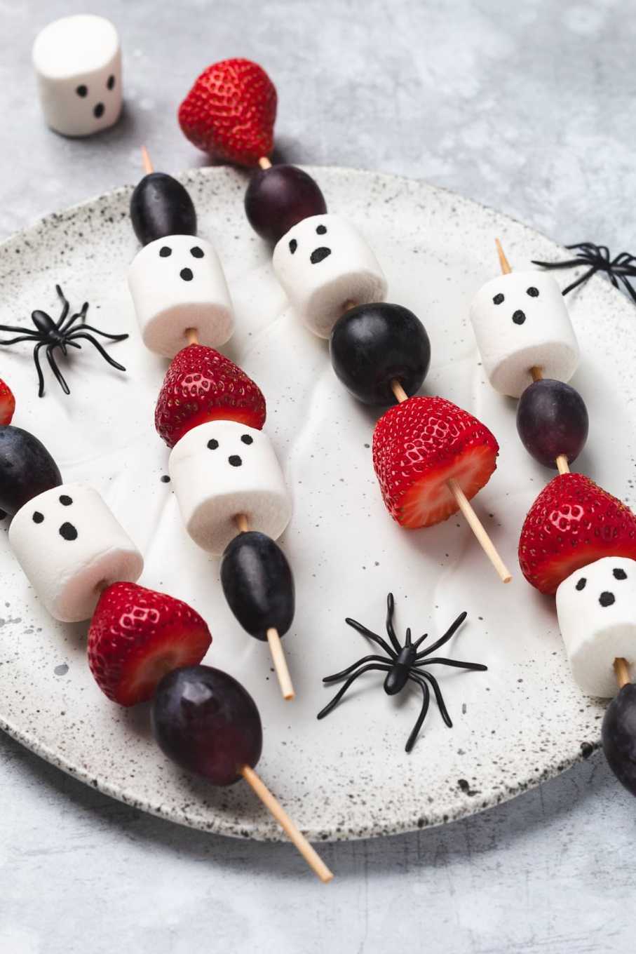 Skewered green grapes with white marshmallow “ghost” heads and chocolate chip eyes, arranged on a platter.
