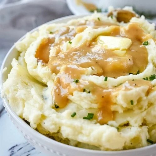 Creamy buttery mashed potatoes with gravy, melted cheese, roasted garlic, and chives in warm bowl
