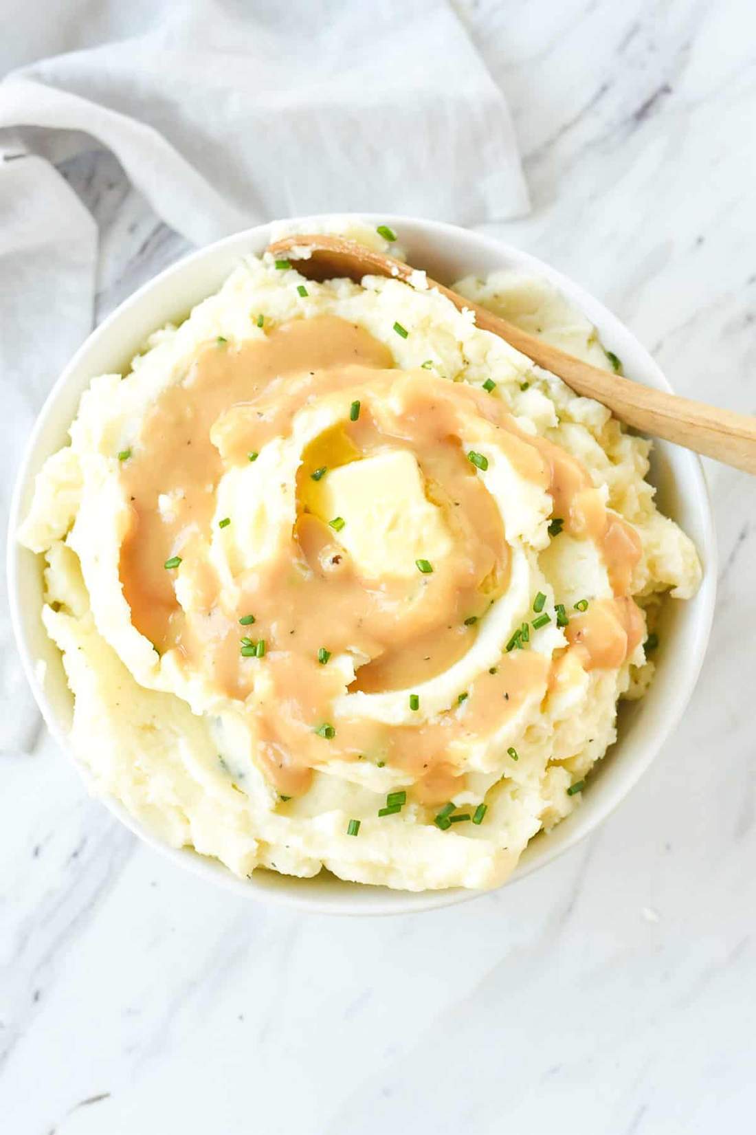 Creamy buttery mashed potatoes with gravy, roasted garlic, melted cheese, and chives in warm bowl