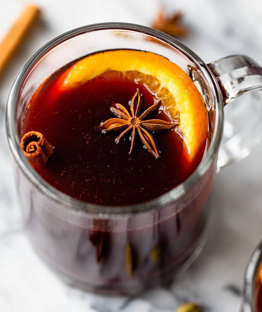 Slow cooker spiced red wine garnished with fragrant orange wheels, ruby-red wine, and cinnamon in rustic mugs.