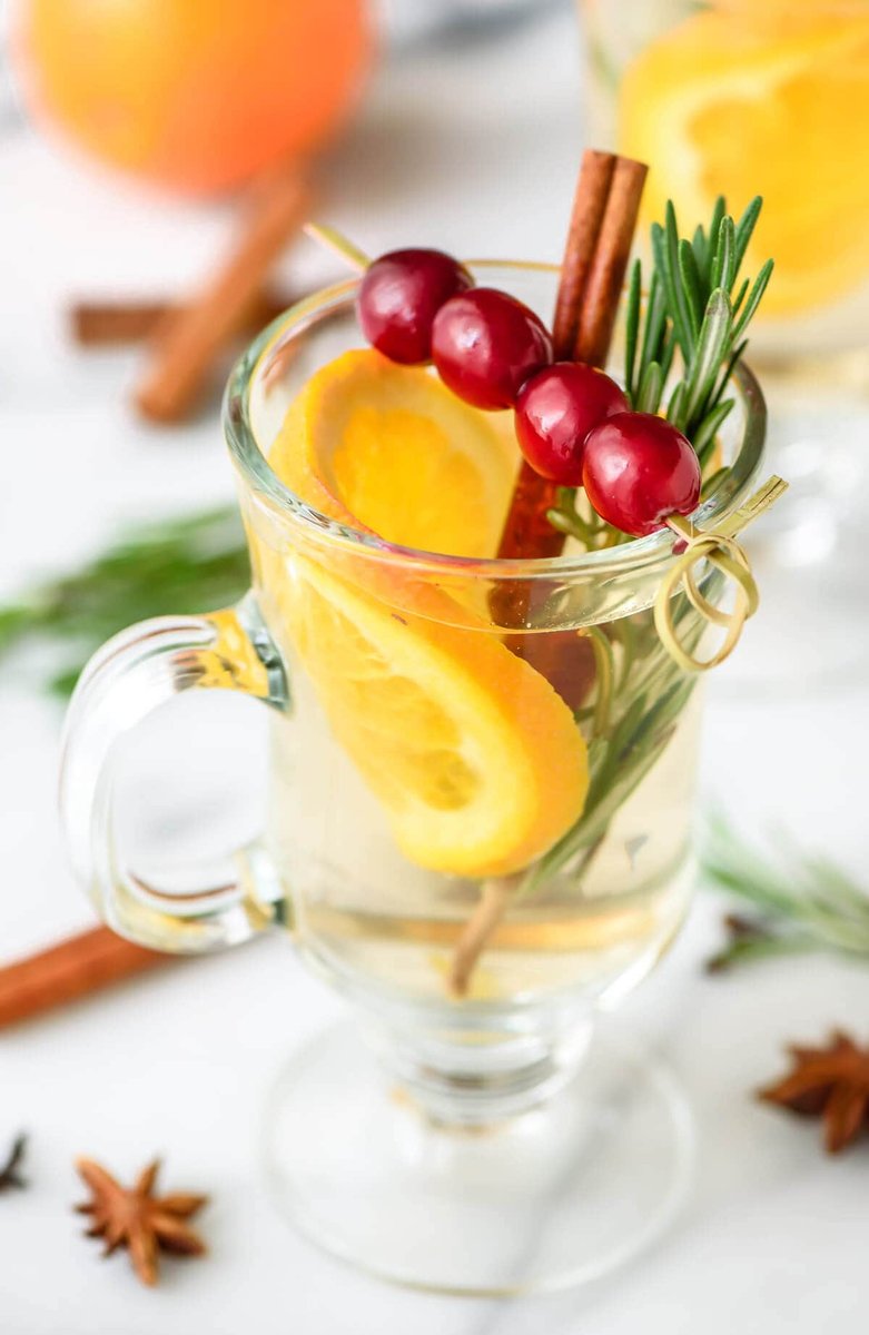 Warm orchard apple mulled white wine with cinnamon, crisp apple slices, and orange in glass mugs.