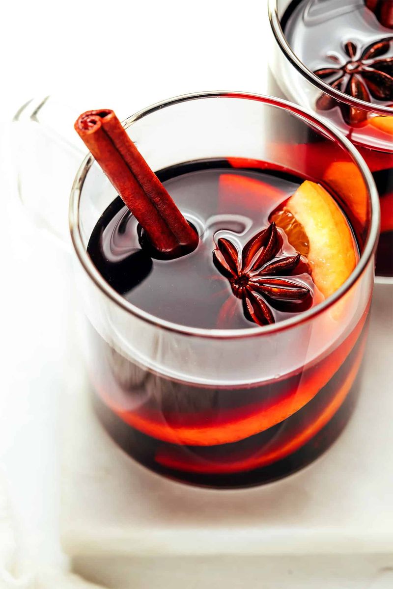 Seville orange mulled wine featuring deep ruby-red wine, spiced citrus slices, and cinnamon sticks in mugs.