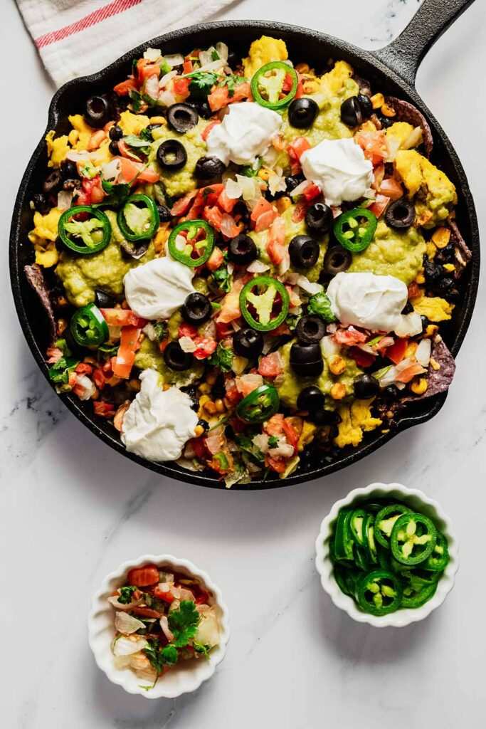Brunch breakfast nachos with fluffy scrambled eggs, crispy bacon, melted cheese, jalapeños, and loaded tortilla chips