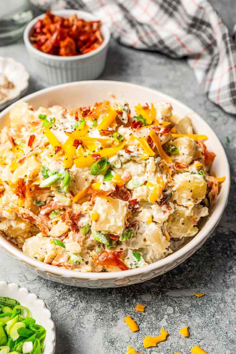 Loaded baked potato salad with creamy dressing, bacon, cheddar, chives, and crispy onions, ideal for summer gatherings