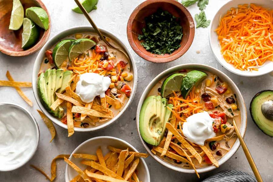 Creamy chicken tortilla soup with sweet corn broth, shredded chicken, crispy tortilla strips, avocado, and lime