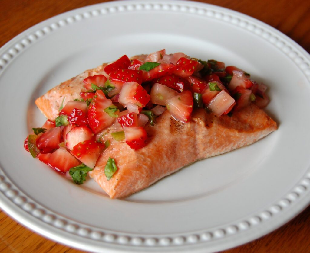 Grilled salmon topped with strawberry salsa, garnished with lime wedges and cilantro
