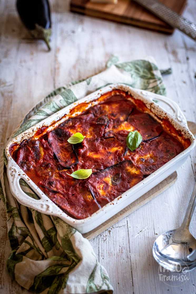 Layered eggplant parmesan with visible slices of eggplant, marinara sauce, and melted mozzarella in a glass baking dish.
