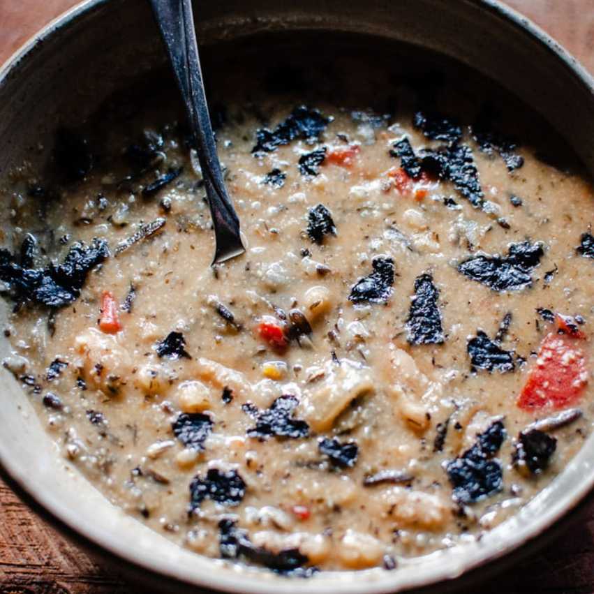 Rich mushroom soup with wild rice and cream, garnished with thyme and a swirl of cream in a bowl.