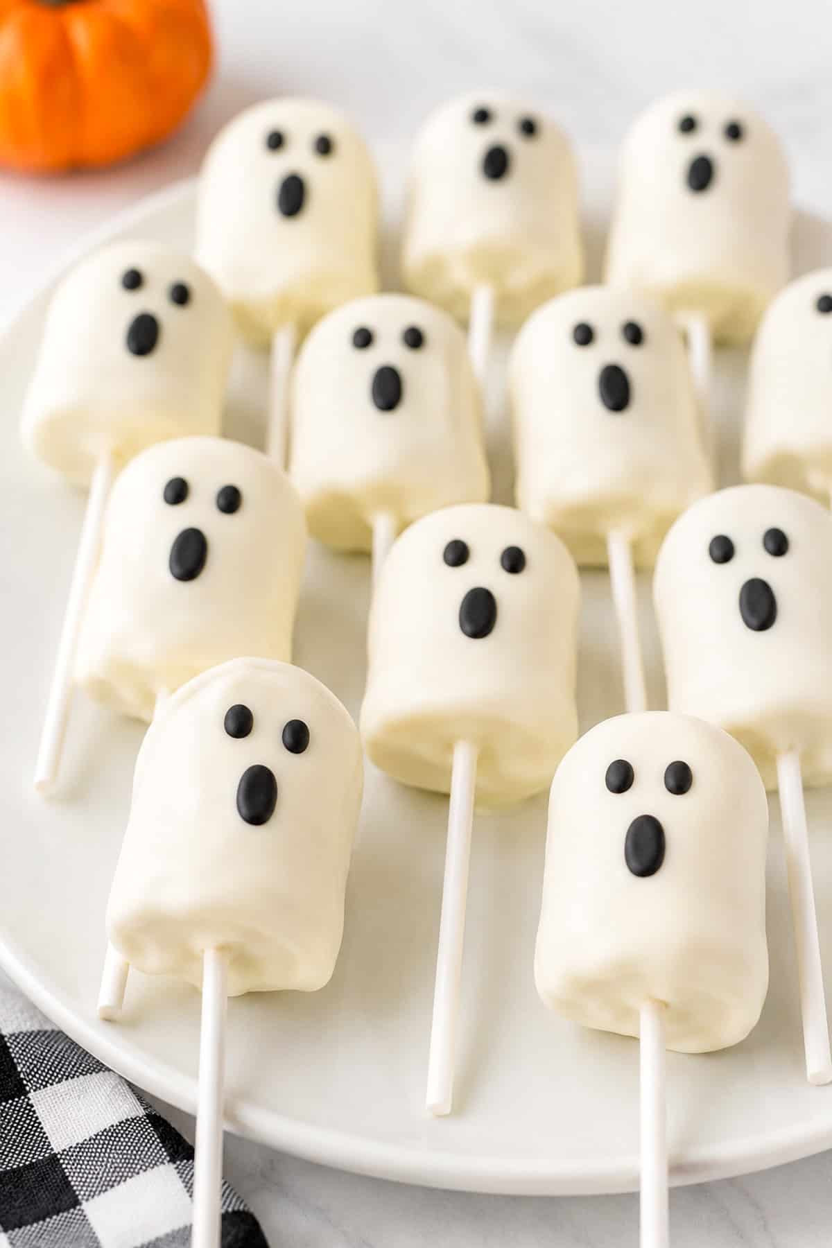 White marshmallows dipped in white chocolate with black chocolate eyes and mouths on wooden sticks.